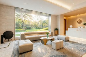 A modern living room with a sofa, ottomans, a coffee table, and a view of a garden through large windows. - Easy Go Inn (Shanghai Hangtou Hunan Highway Store) (Shanghai)