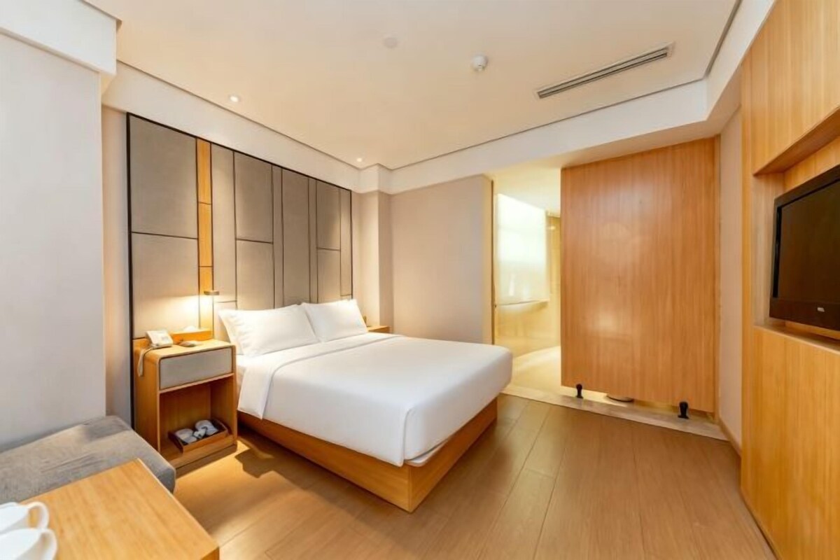 A modern hotel room with a large bed, bedside table, and a TV mounted on the wall.
