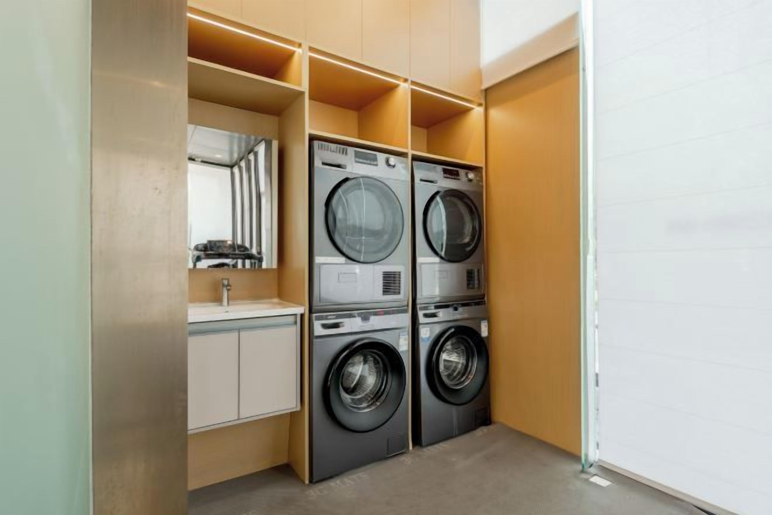 A laundry room with two stacked washing machines, a mirror, and a sink.
