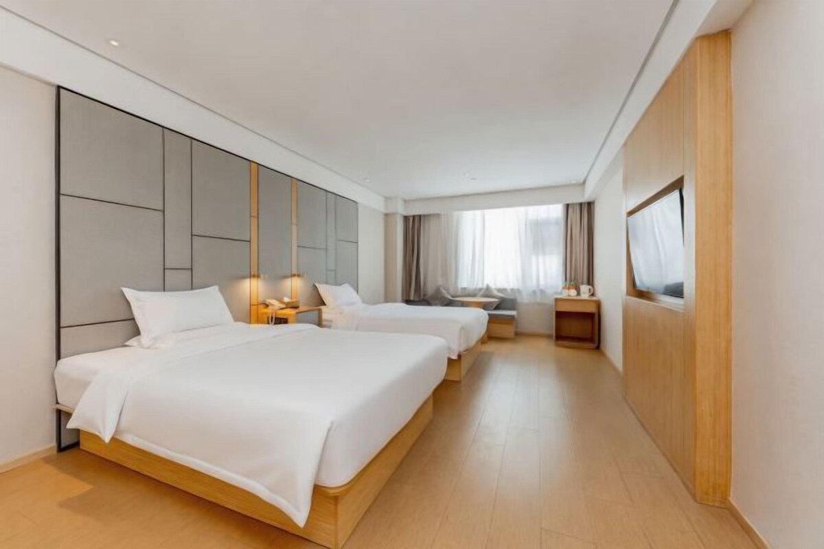 A hotel room with two beds, a large mirror, and a wooden floor.