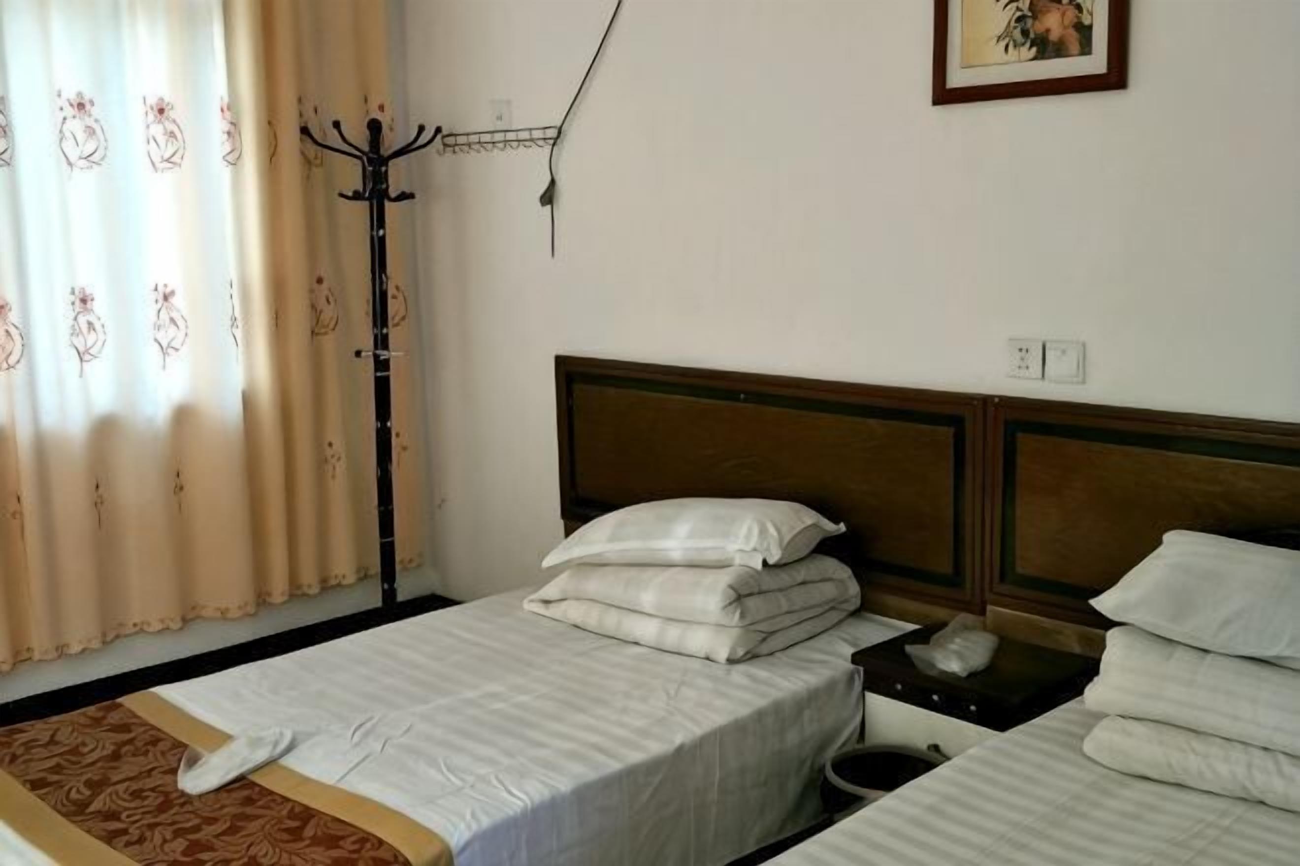 Une chambre d’hôtel avec deux lits, une table de chevet, une lampe et une fenêtre avec des rideaux.
