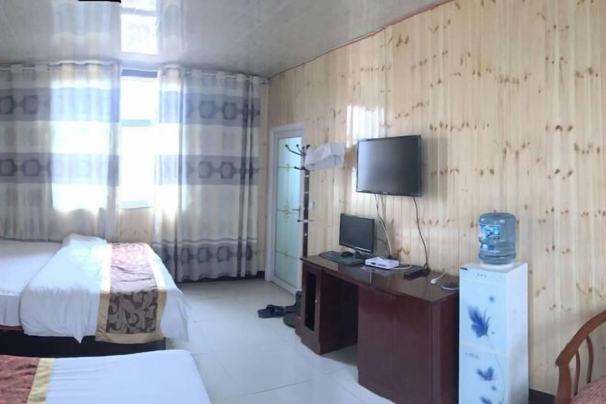 A hotel room with two beds, a TV, a desk with a computer, and a water dispenser.