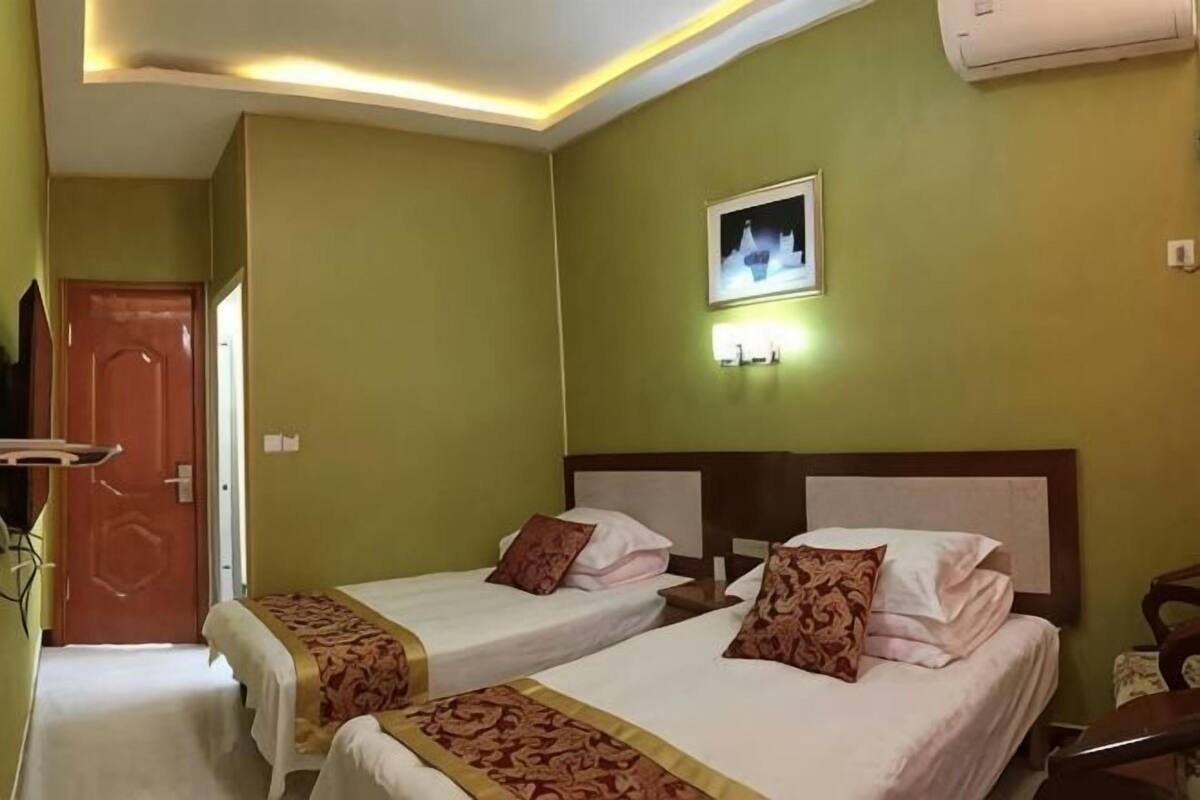 A hotel room with two beds, a door, a wall-mounted light, and an air conditioner.