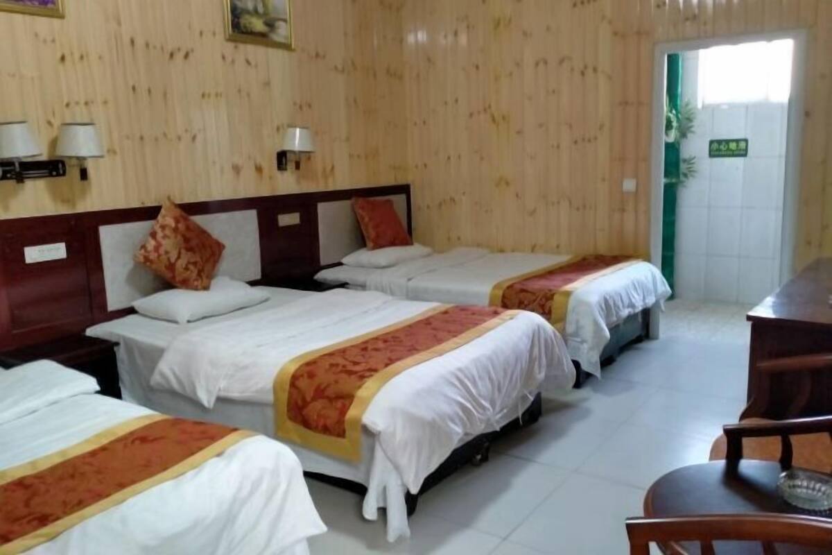 A hotel room with three beds, wooden walls, and a desk with a chair.