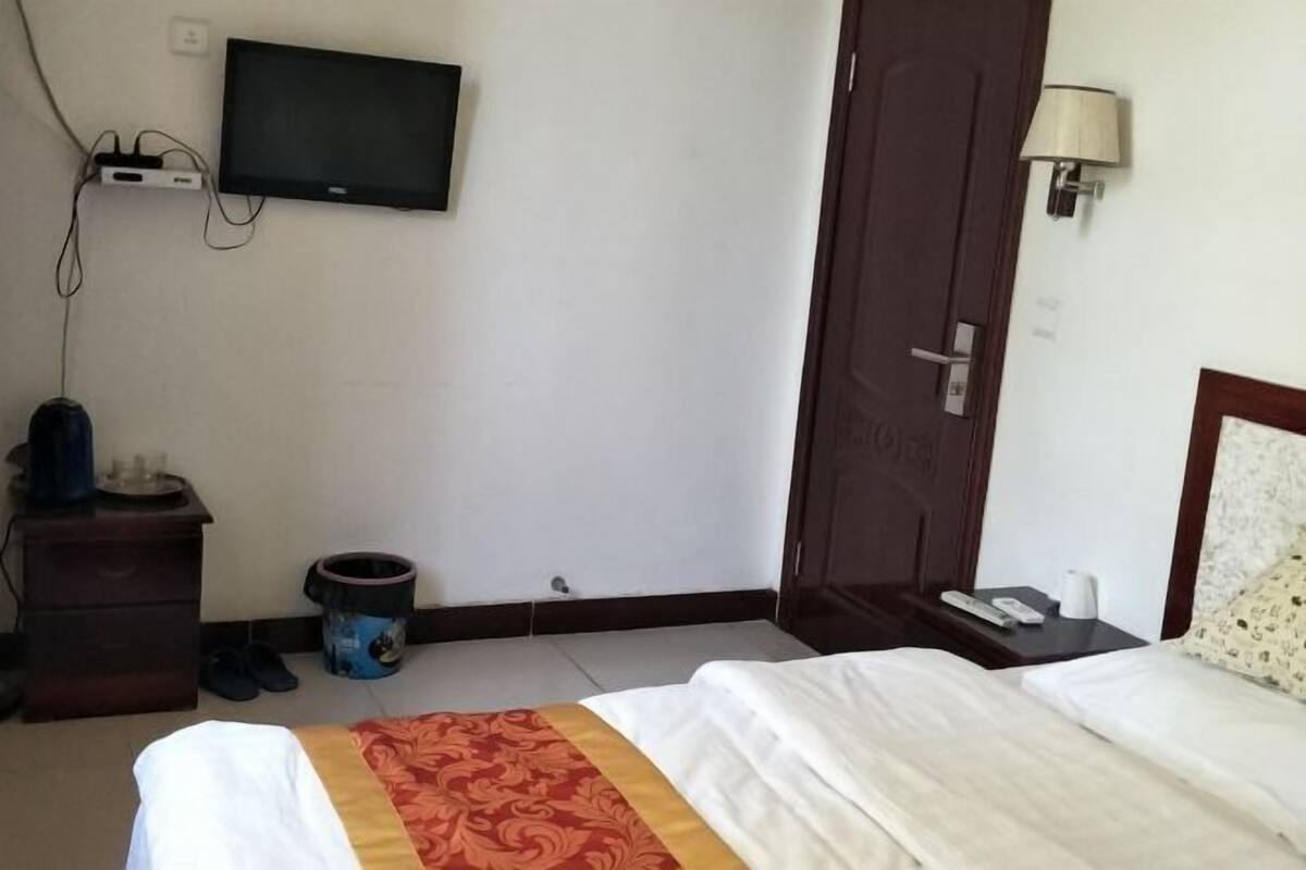 A hotel room with a bed, a television mounted on the wall, a bedside table with a lamp, and a door.