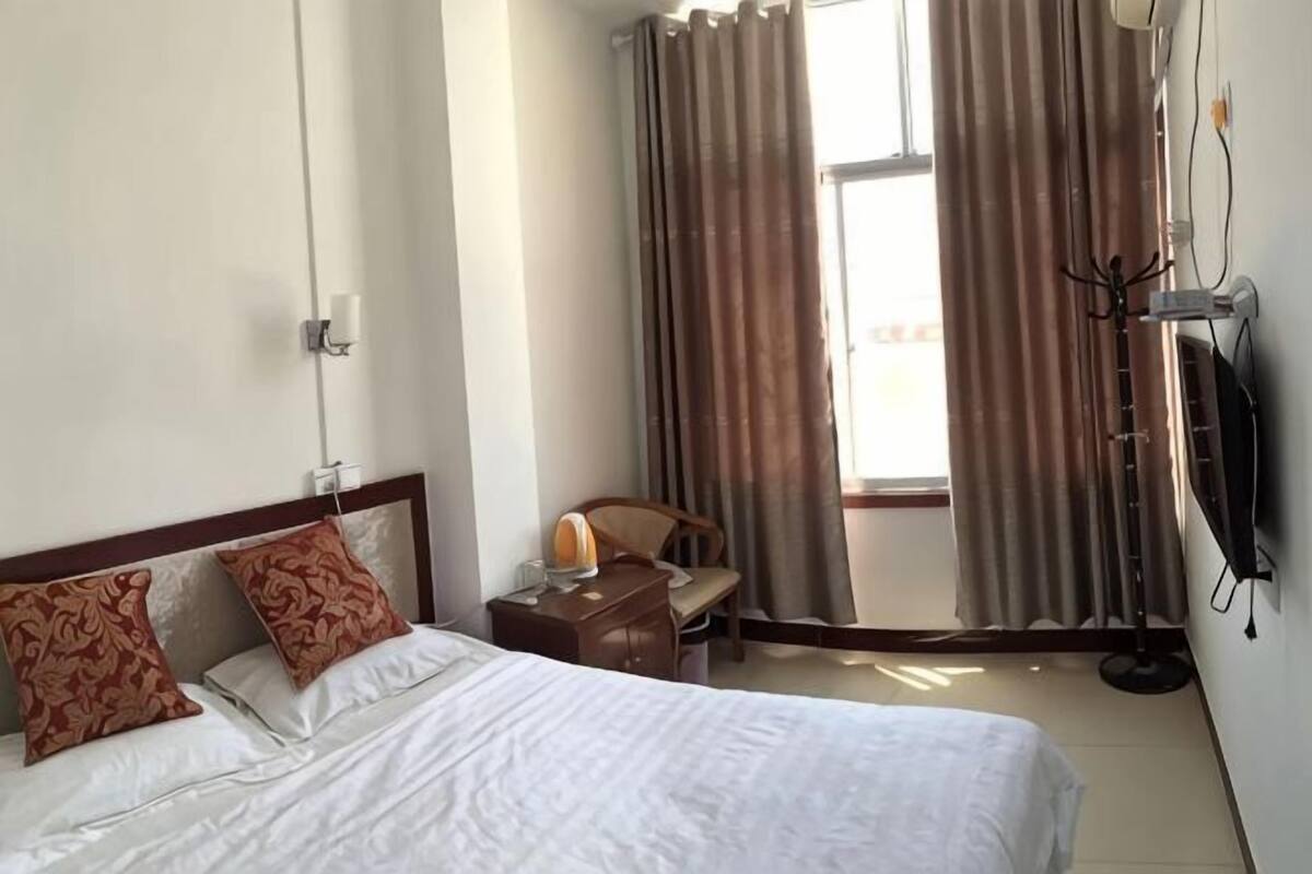 A hotel room with a bed, a desk, a chair, a TV, and a window with curtains.