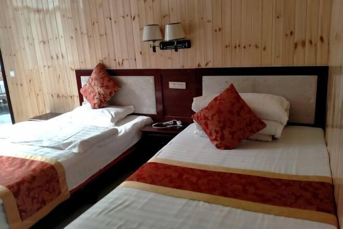 A hotel room with two beds, each with a pillow and a bedside table. There are wall-mounted lamps above the beds.