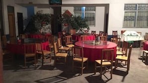 Un espace repas avec des tables rondes recouvertes de nappes rouges, des chaises en bois et des plantes en pot.