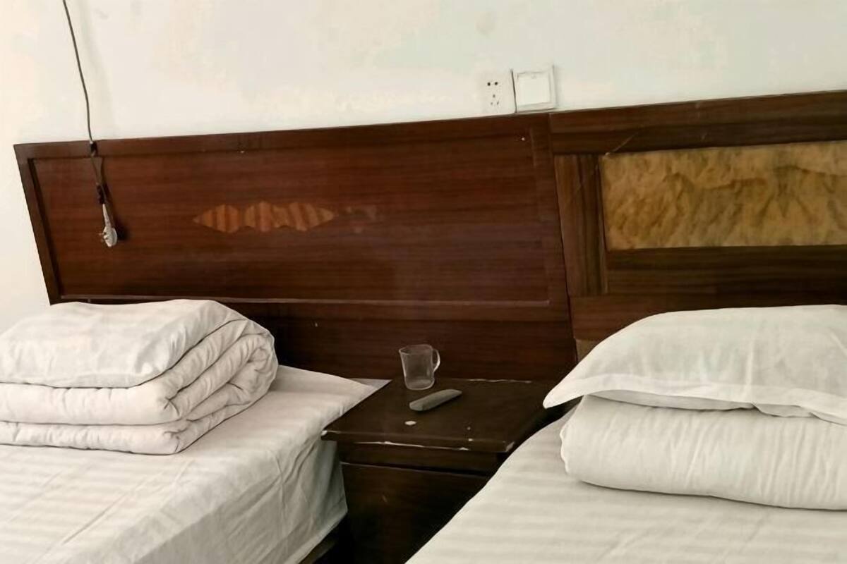 A hotel room with two beds, a wooden headboard, a bedside table with a glass, and a remote control.