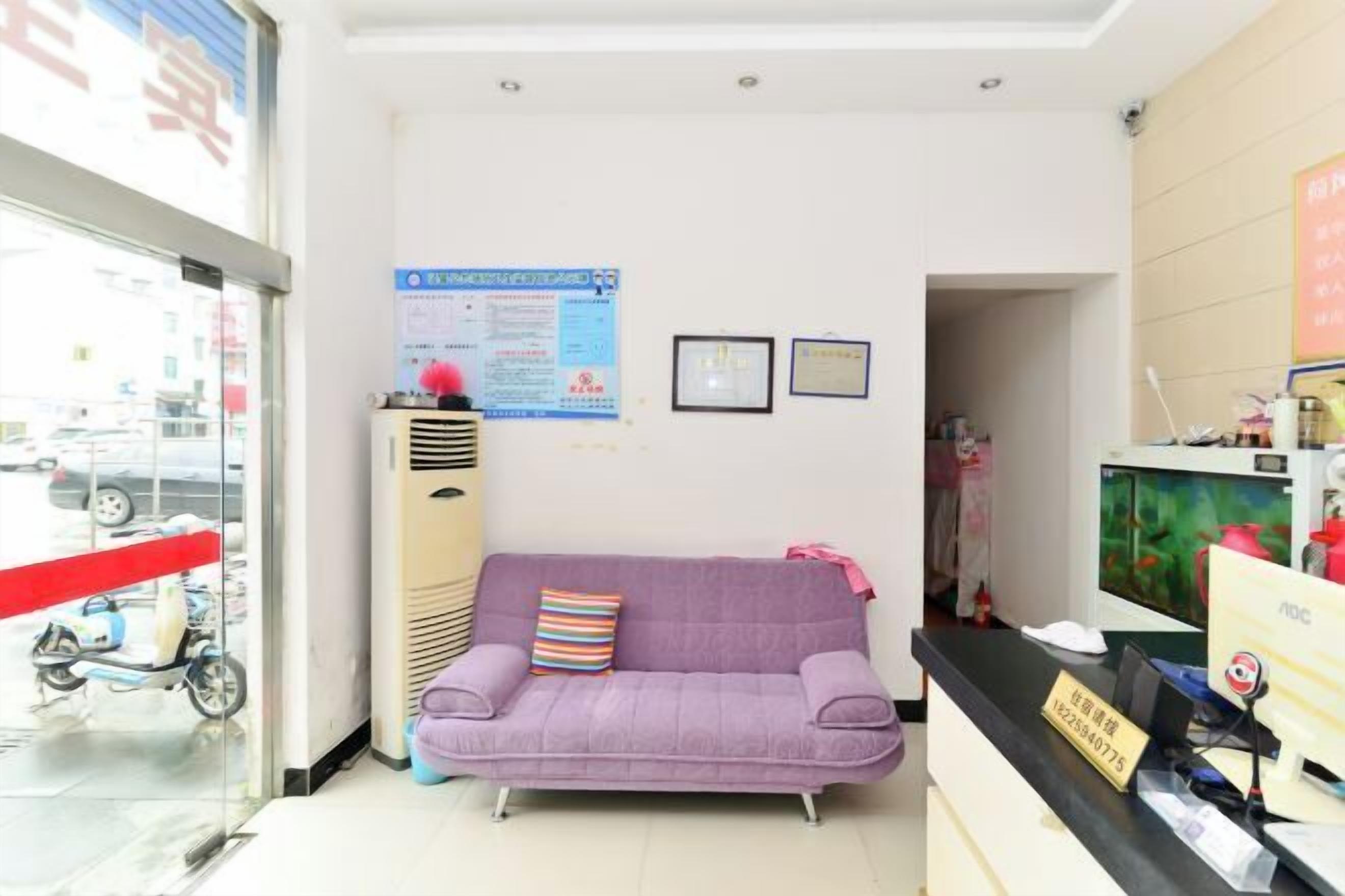A reception area with a purple sofa, a computer desk, and a wall-mounted air conditioner.