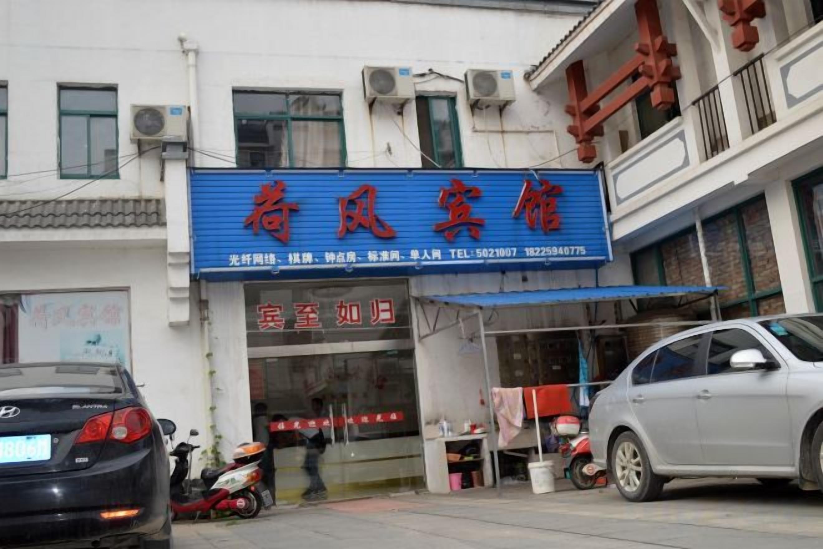 A hotel with a blue signboard, a visible entrance, and a parked car.