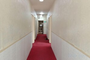 A narrow hallway with a red carpet leading to a room with a bed and a nightstand. - Hefeng Hotel (Jing County)