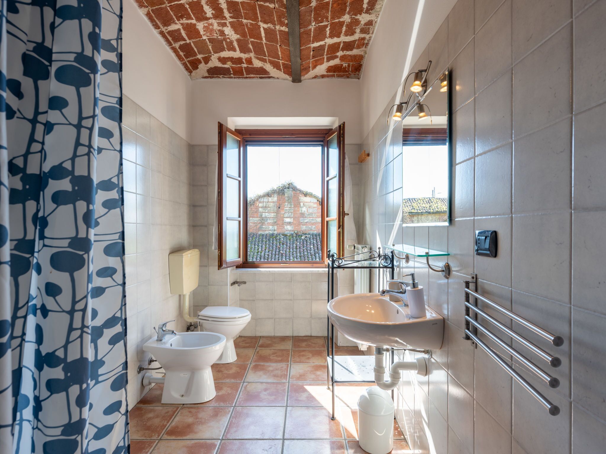A bathroom with a window, two toilets, a sink, and a shower.