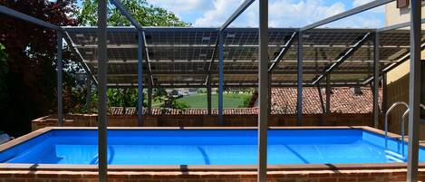 A swimming pool with a metal roof structure and solar panels.