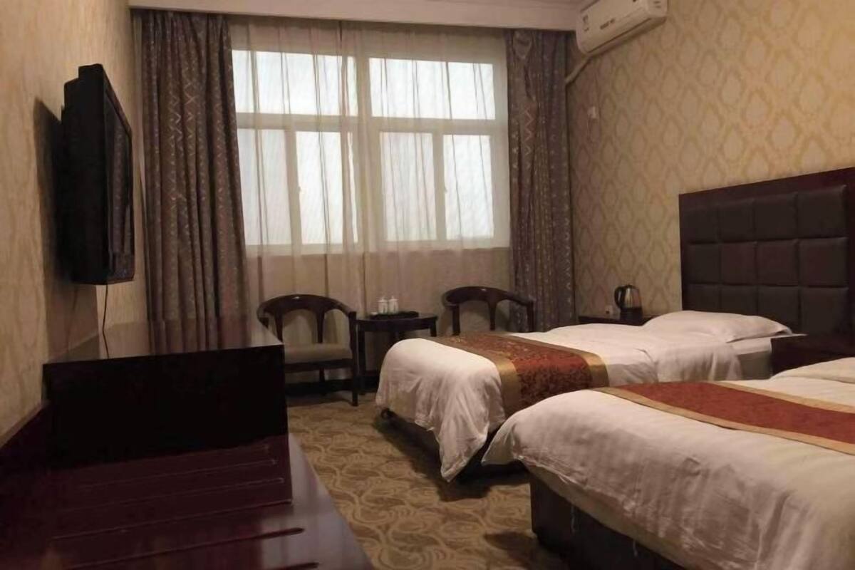 Habitación de hotel con dos camas, televisión, escritorio y ventana con cortinas.