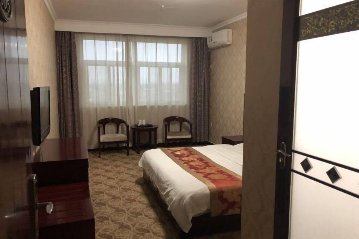 Una habitación de hotel con una cama, dos sillas, una mesita y un equipo de aire acondicionado.