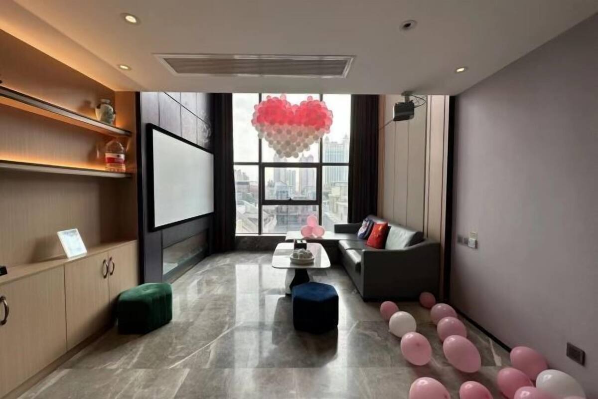 A modern hotel room with a large window, a sofa, a coffee table, and a green ottoman.