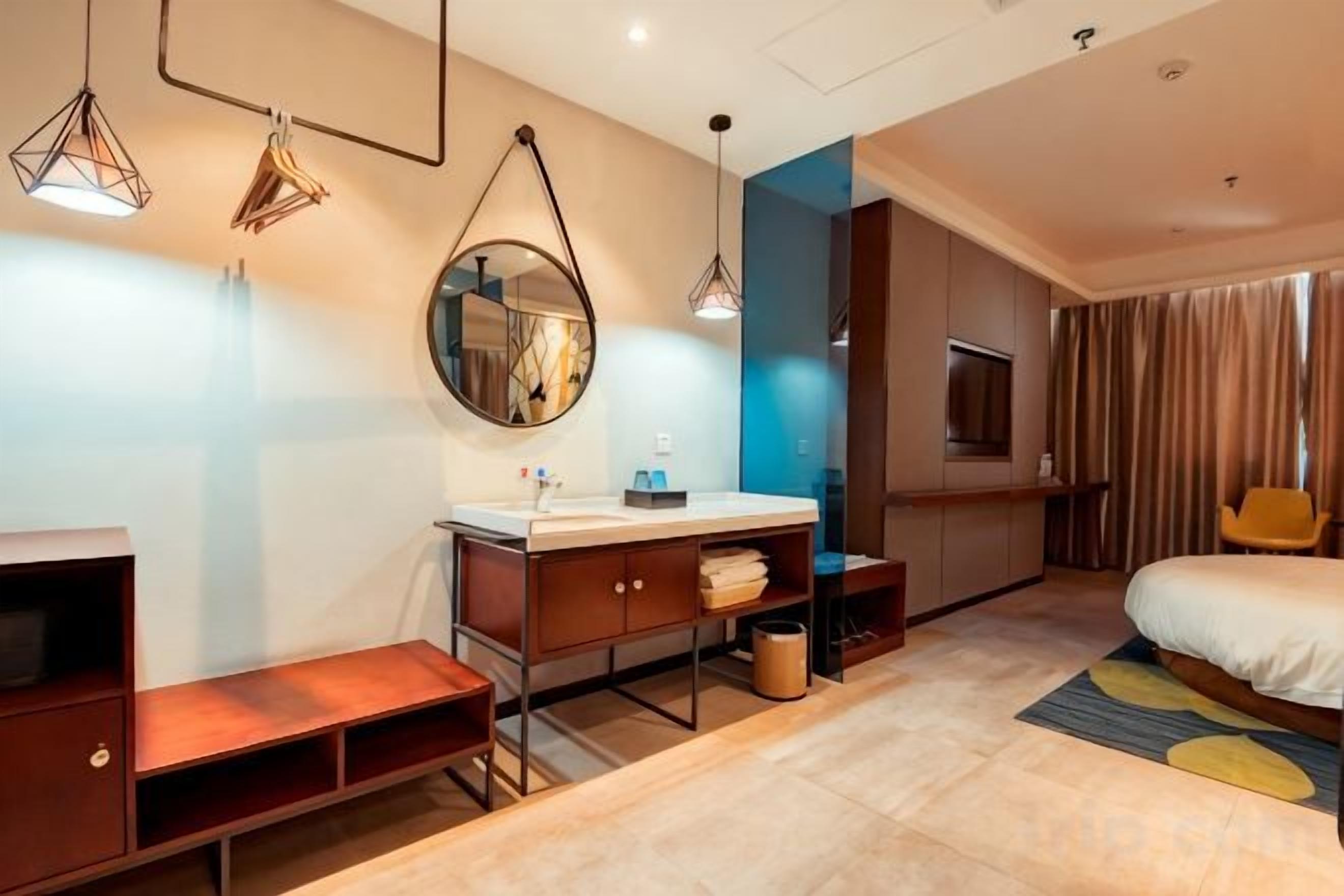 A modern hotel room with a bed, a desk, a mirror, and a TV.