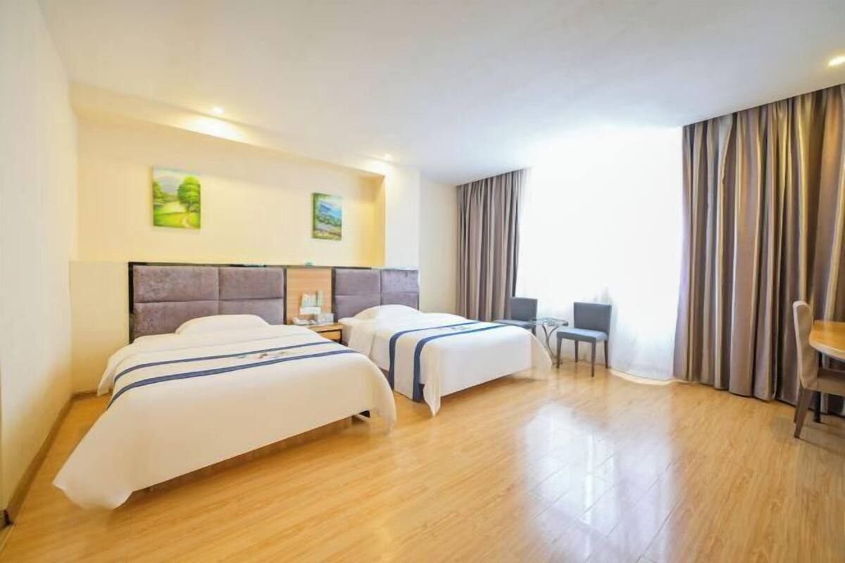 A hotel room with two beds, a desk, a chair, and a window with curtains.