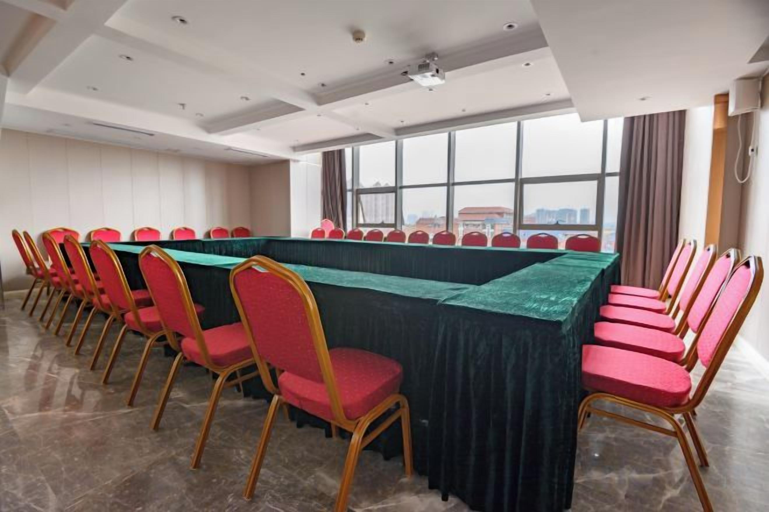A conference room with a long table, red chairs, and a view through large windows.