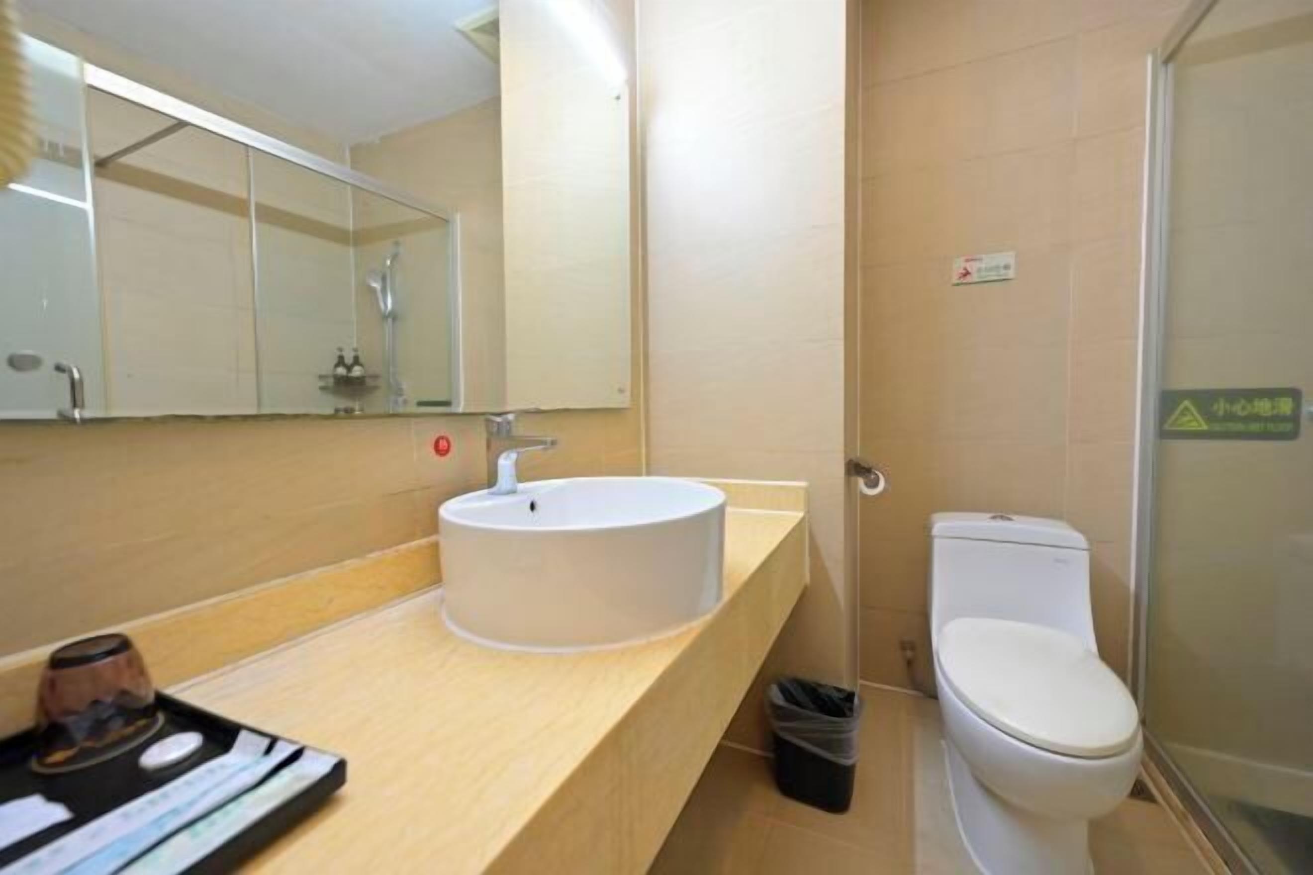 A bathroom with a white sink, a mirror, a toilet, and a trash bin.