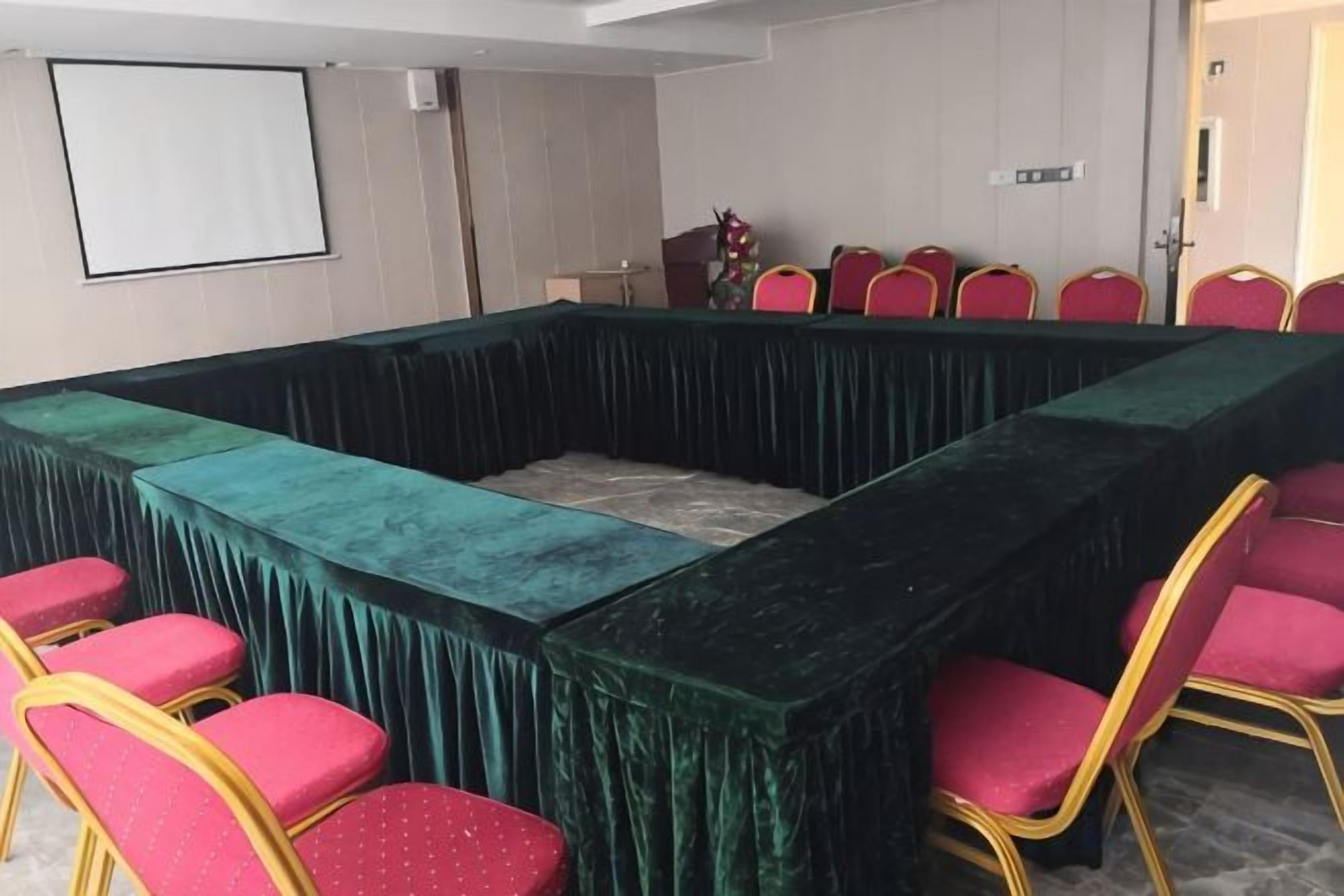 A conference room with a long table, red chairs, and a projector screen.