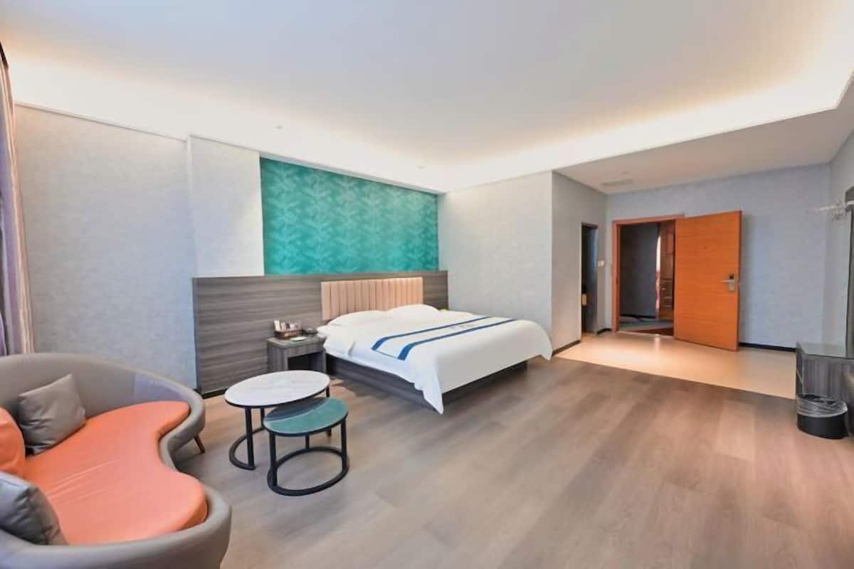 A modern hotel room with a bed, a curved sofa, a small round table, and a door leading to another room.