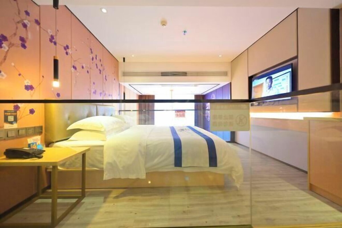 A hotel room with a bed, a desk, a television, and a wall with a floral design.