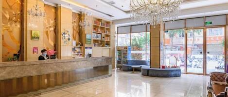 A hotel lobby with a reception desk, a chandelier, and a seating area.