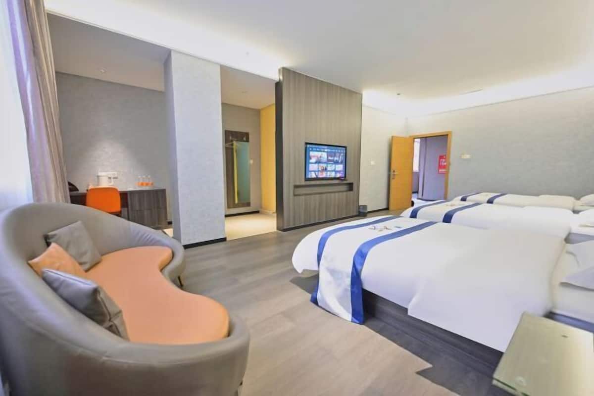A hotel room with a curved sofa, a TV mounted on the wall, and a bed with a blue and white bedspread.