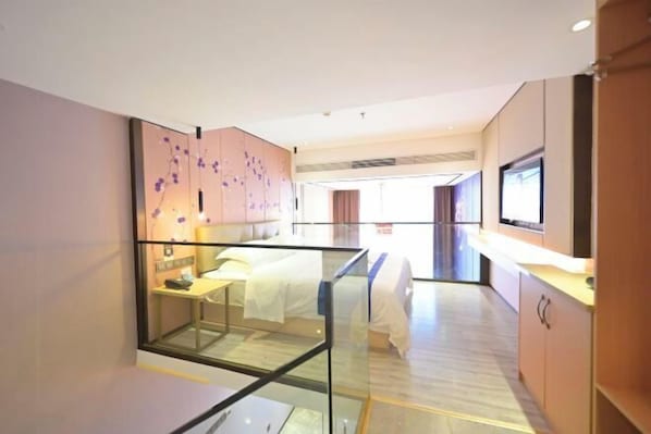 Une chambre d’hôtel moderne dotée d’une paroi en verre, d’un lit, d’un bureau et d’un téléviseur.