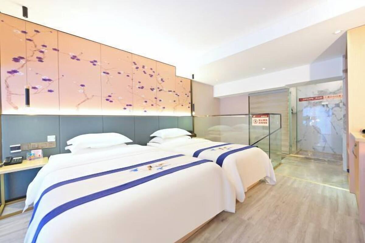 A hotel room with two beds, a desk, and a glass door leading to a bathroom.