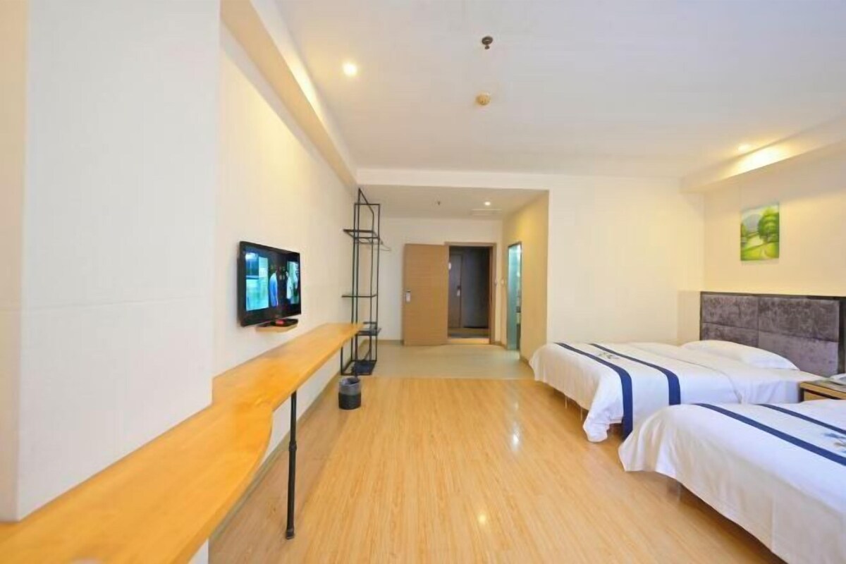 A hotel room with two beds, a TV, a wooden bench, and a hallway leading to another room.