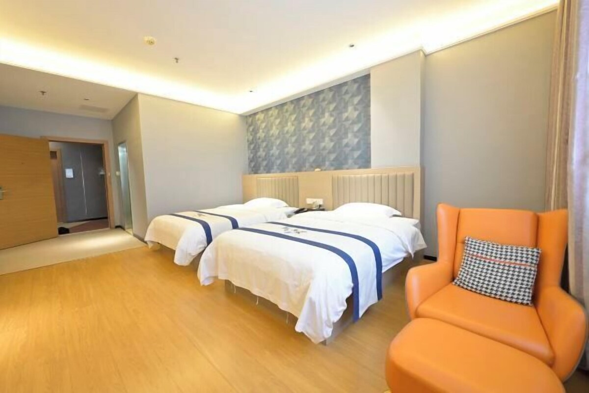 A hotel room with two beds, a wooden floor, a radiator, and an orange armchair.