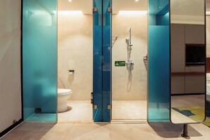 Douchecabine met glazen wanden, waarin een toilet zichtbaar is, met douchekop en een waarschuwingsbord voor een natte vloer.