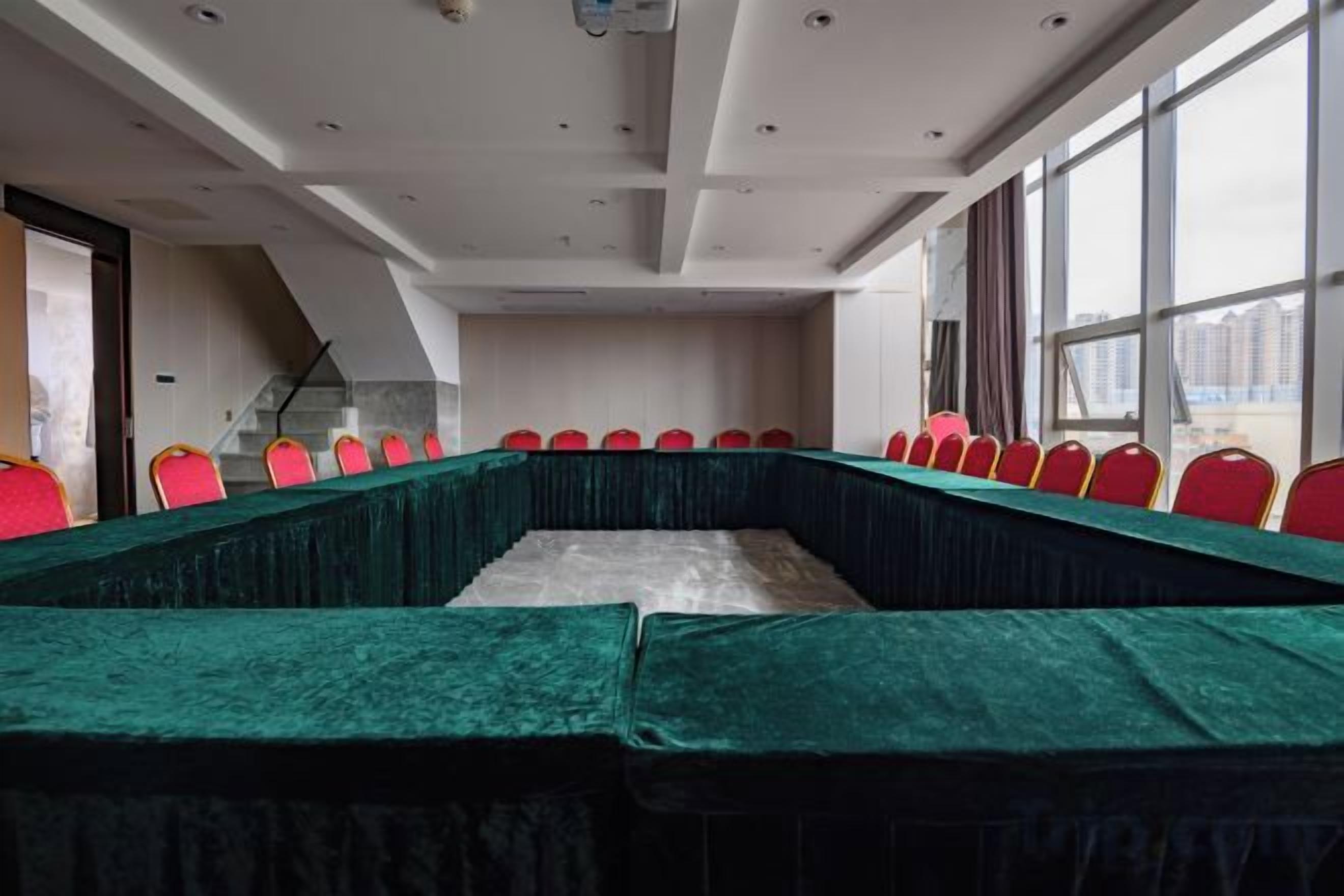 A conference room with a long table, red chairs, and large windows.