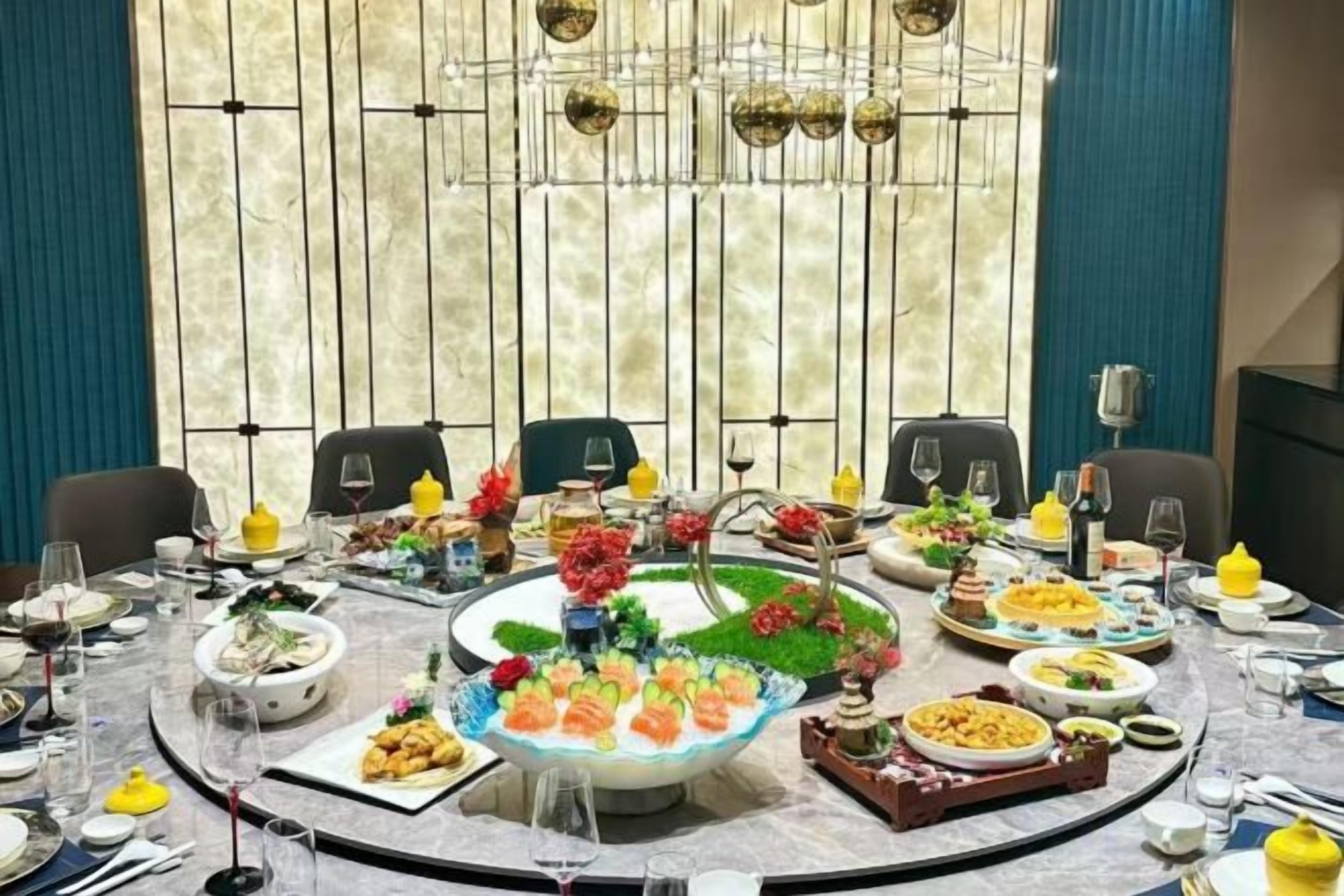 Mesa redonda de comedor con diversos platos y bebidas, rodeada de sillas.
