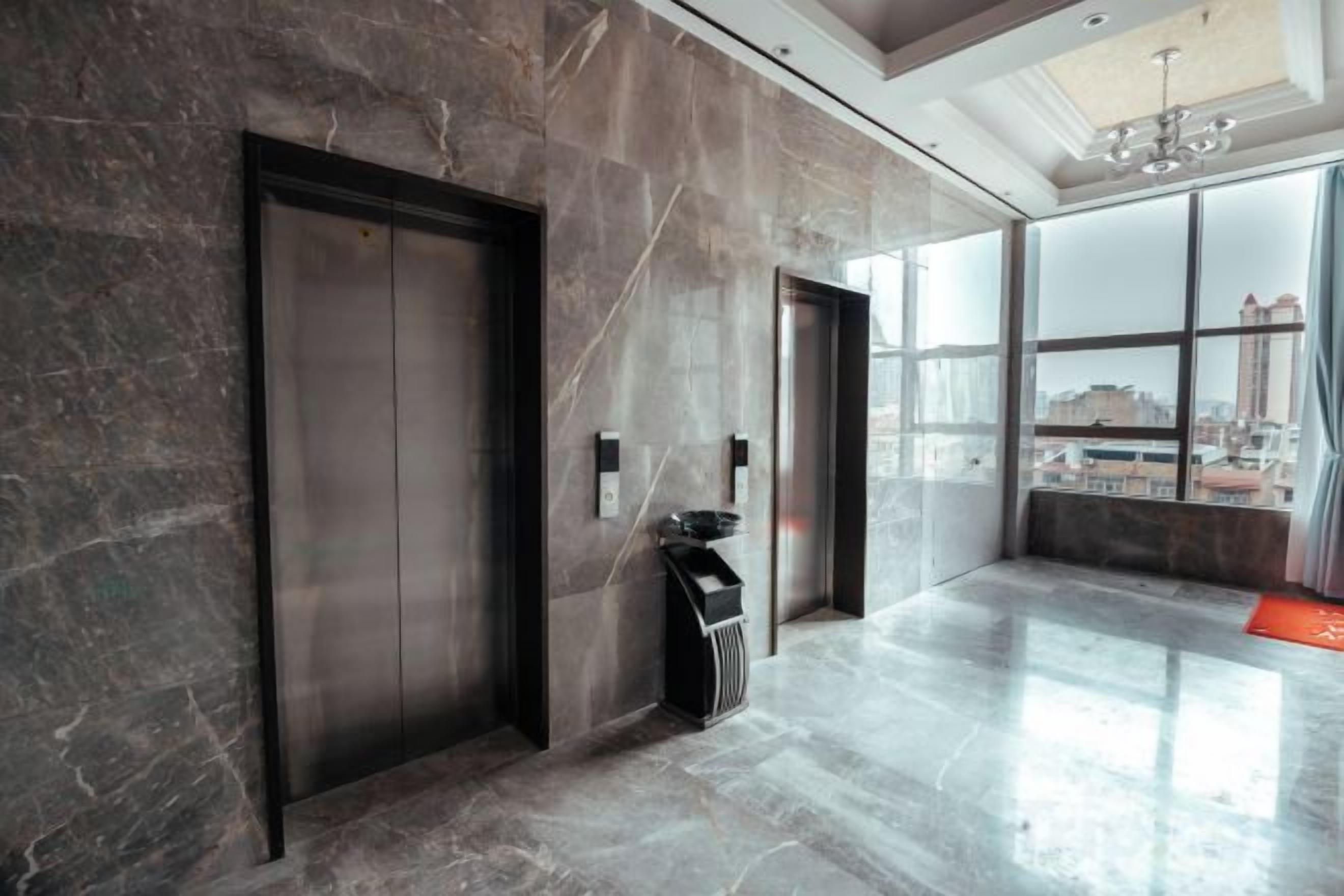 Un ascensor moderno con detalles metálicos, puerta de vidrio y un pequeño cubo de basura a un lado.