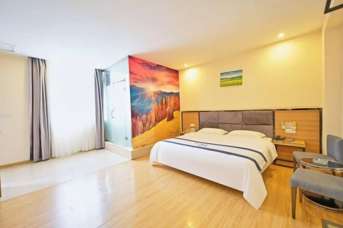 A hotel room with a bed, a desk, a chair, a painting on the wall, and a window with curtains.