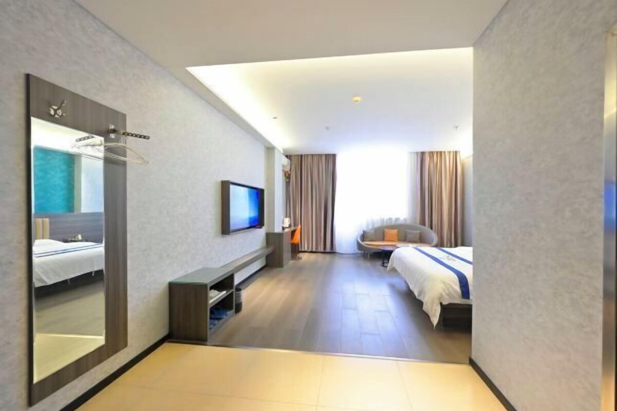 A modern hotel room with a large mirror, a flat-screen TV, a sofa, and two beds.
