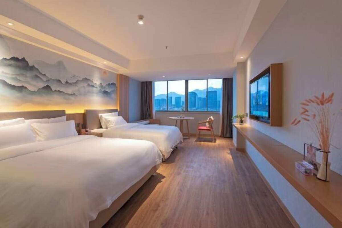 A hotel room with two beds, a small table, a chair, a TV, and a city view.