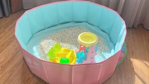 Un parc pour enfants rose et bleu, avec des jouets et un gobelet jaune.