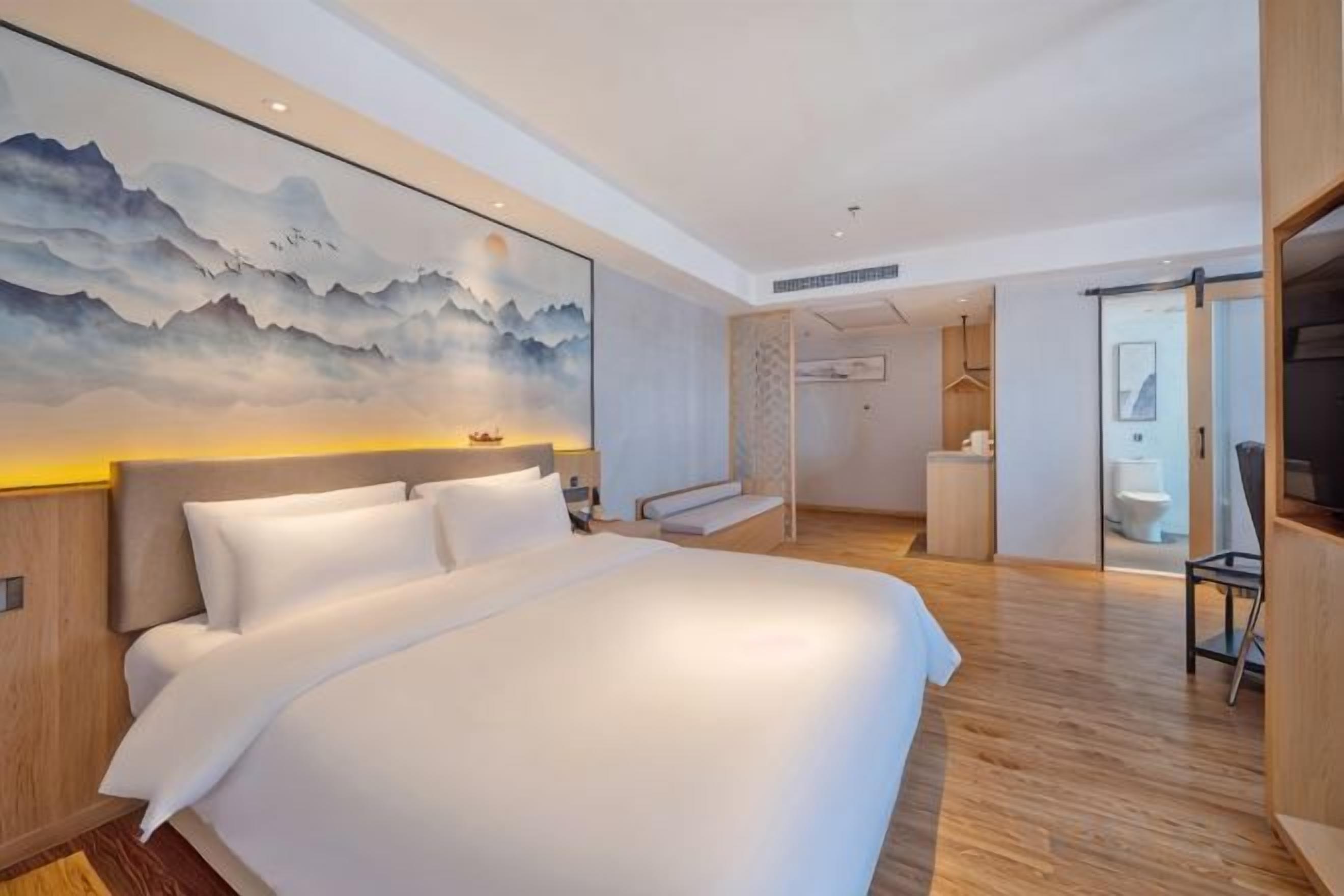 A modern hotel room with a large bed, a painting on the wall, and a view of the bathroom.