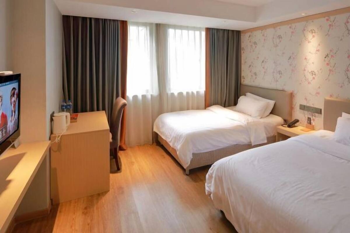 A hotel room with two beds, a desk, a TV, and a window with curtains.