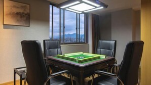 Une salle de conférence avec une table verte, quatre chaises noires, une grande fenêtre donnant sur un paysage urbain et un luminaire fixé au plafond.