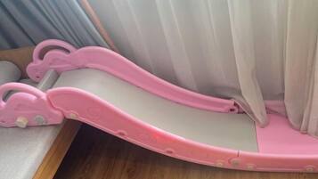 A pink baby walker with a curved design, positioned near a window with white curtains.