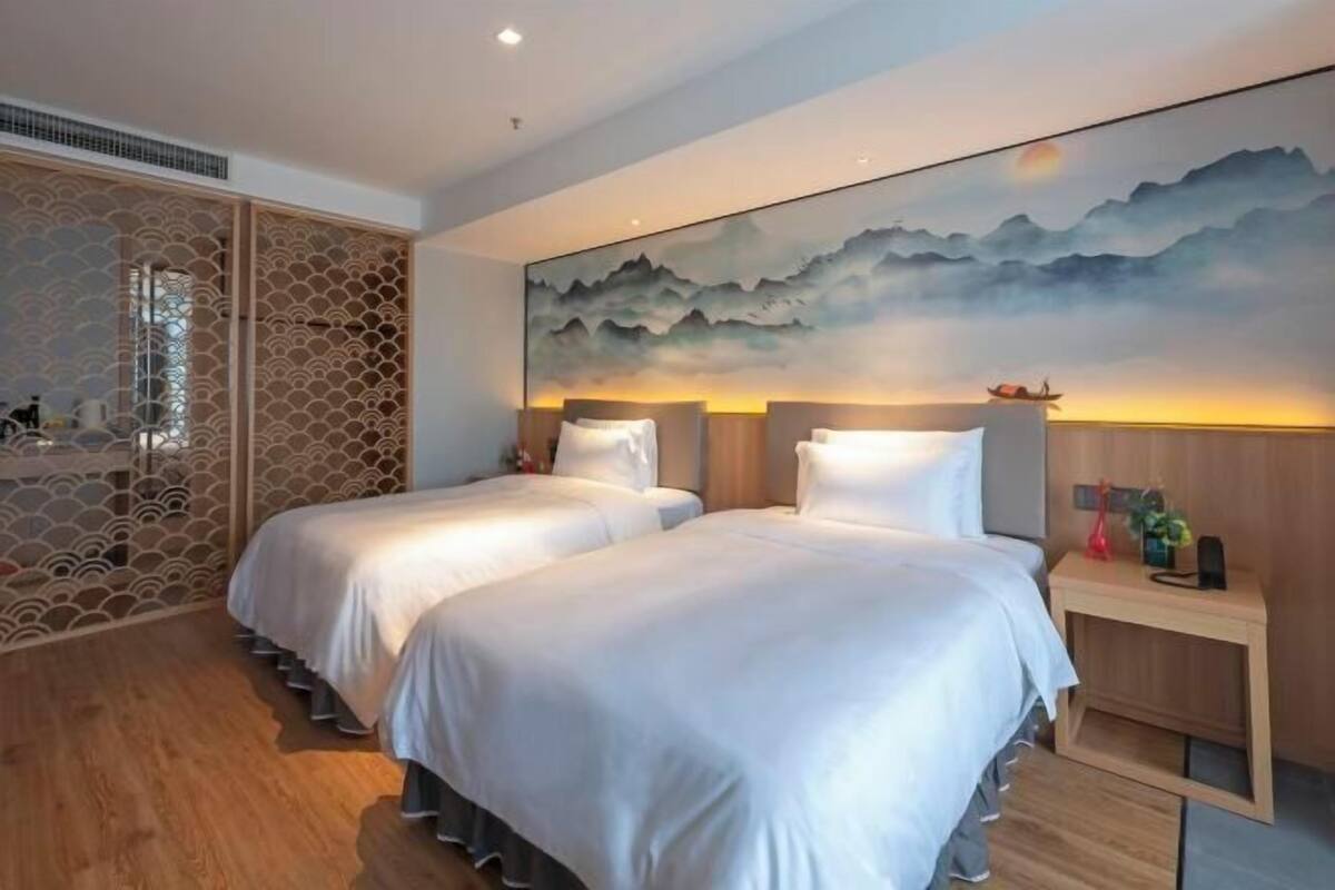 A hotel room with two beds, a large wall painting, a wooden floor, and a decorative screen.