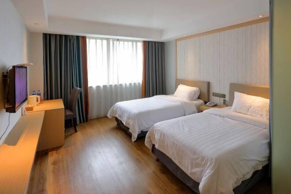 A hotel room with two beds, a desk, a TV, and a window with curtains.