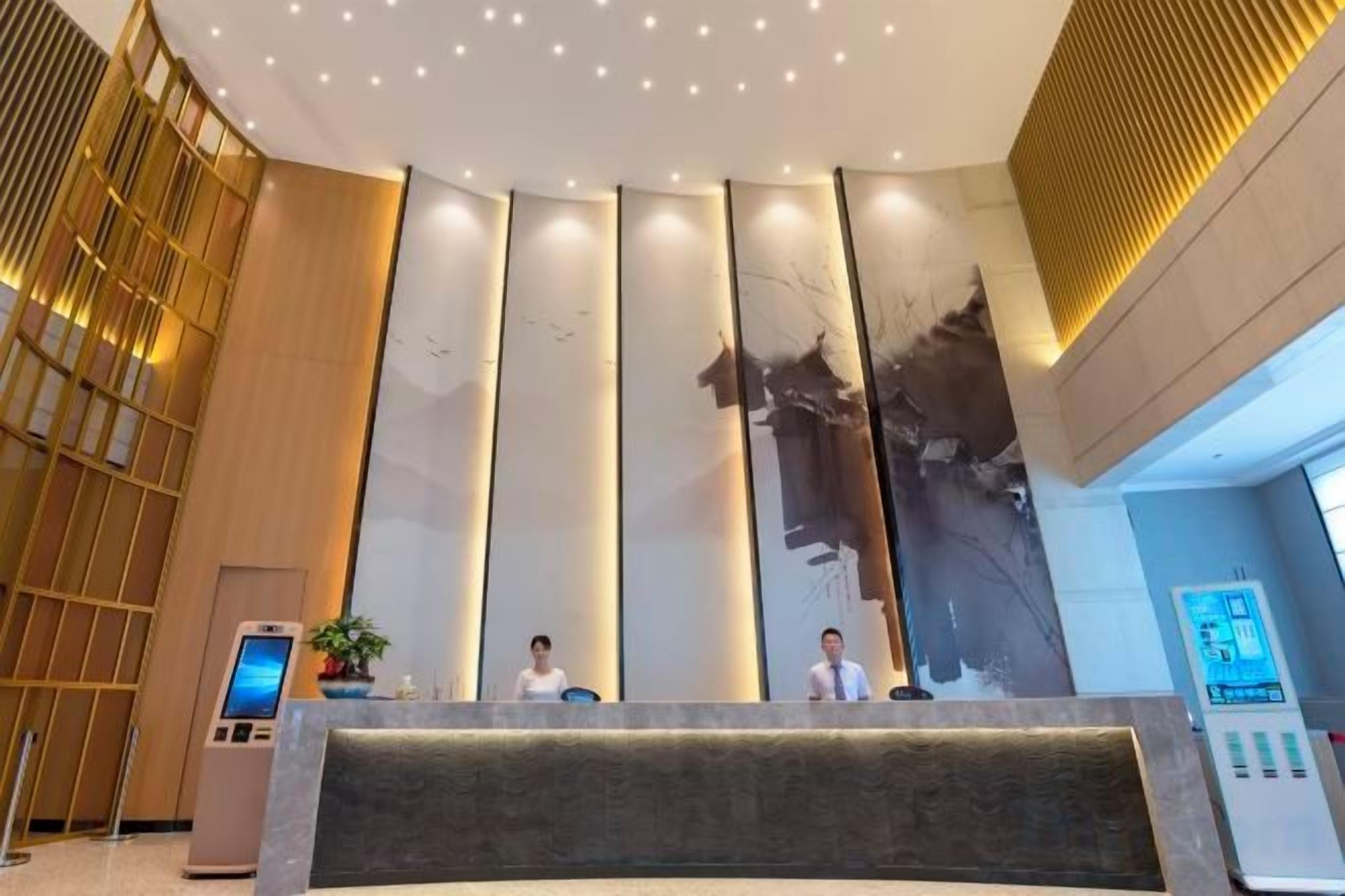 A hotel reception area with a modern design, featuring a reception desk, a large wall with vertical panels, and a seating area.