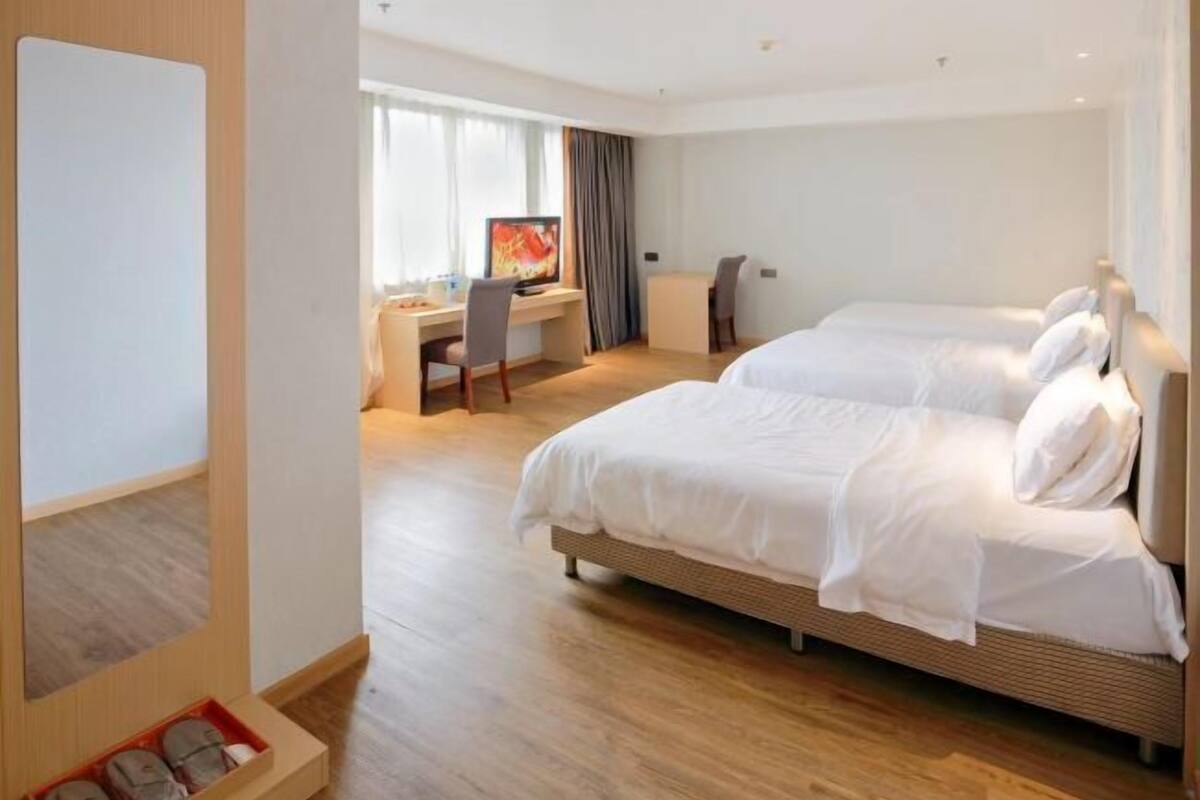 A hotel room with two beds, a desk, a chair, and a television.